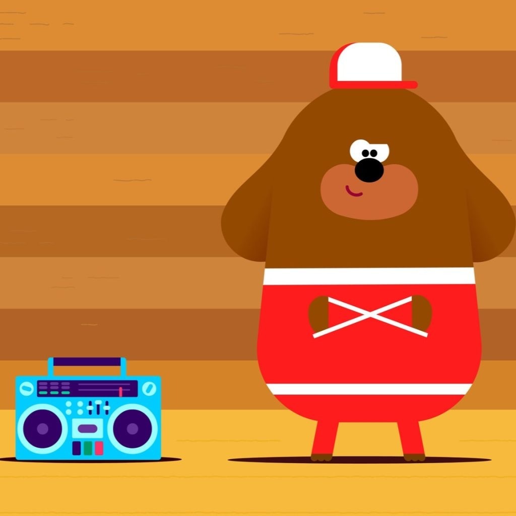 Duggee in tracksuit standing arms crossed next to boombox