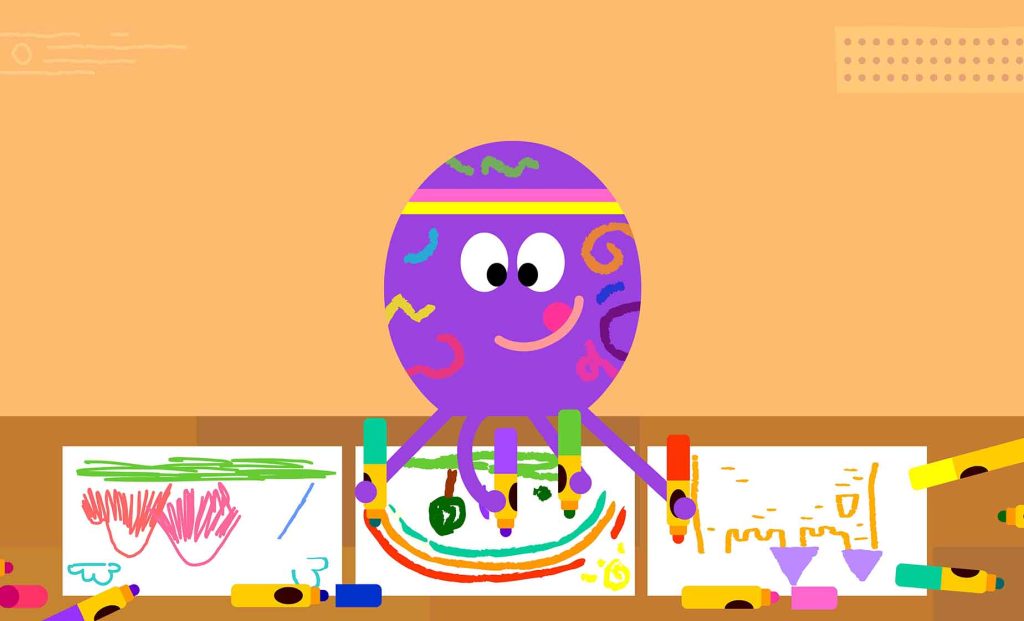 Betty is sat behind a table drawing on three pieces of paper with felt tips held in four of her tentacles.